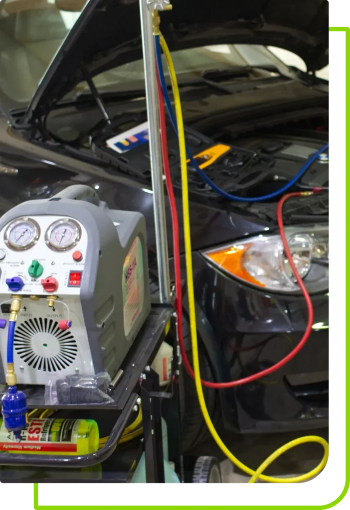 auto ac repair, auto repair in Jacksonville, FL at Mack Motorwerks. Car in a garage with the hood open, connected to a portable AC recharge machine. Red and blue hoses are attached to the vehicle for air conditioning maintenance. Various tools and bottles are visible on the machines cart.